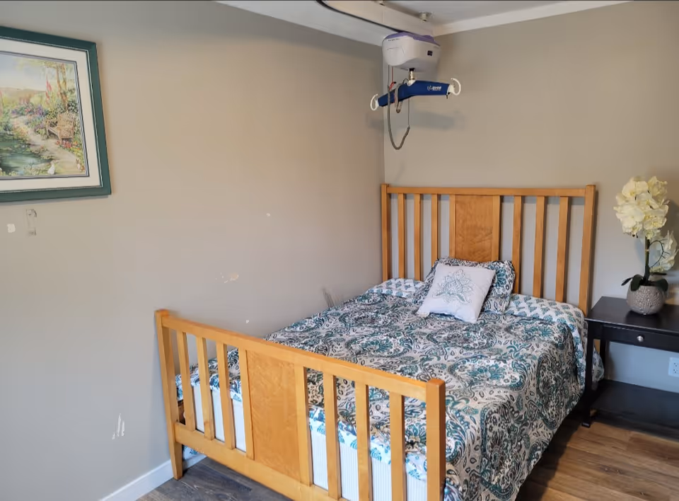 Wood-framed bedroom featuring a patterned bed, nightstand with vase of white flowers.