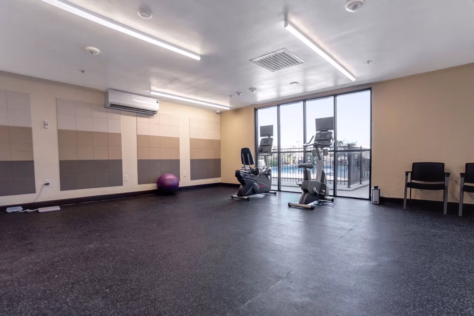 Indoor fitness room with stationary bikes, a purple ball, and large windows.