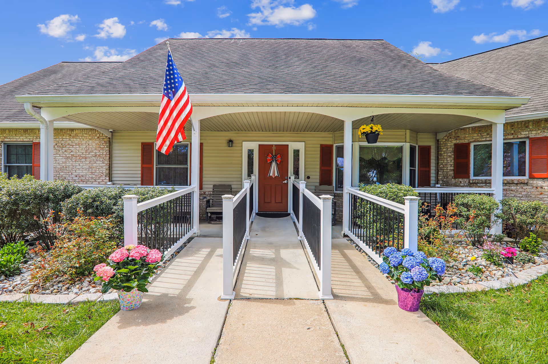 Front entrance of a single-story senior living facility with American flag and flower planters.