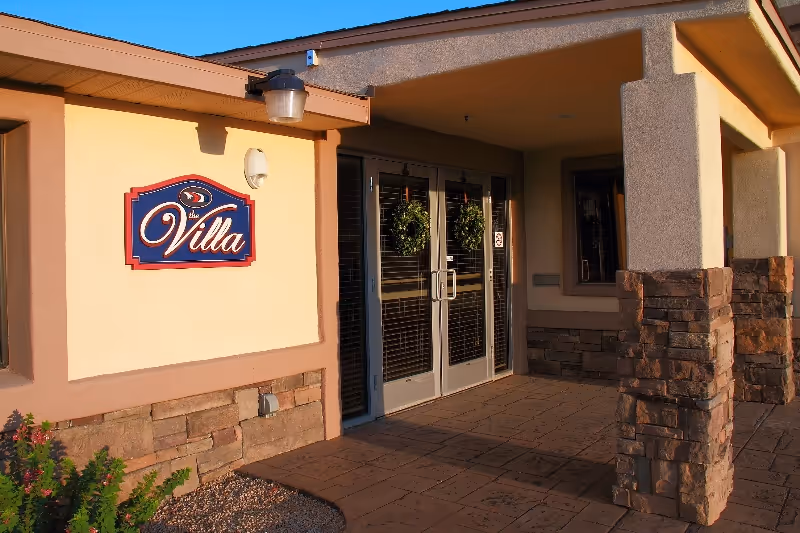 Exterior entrance of a villa-style senior facility with double doors and stone columns.