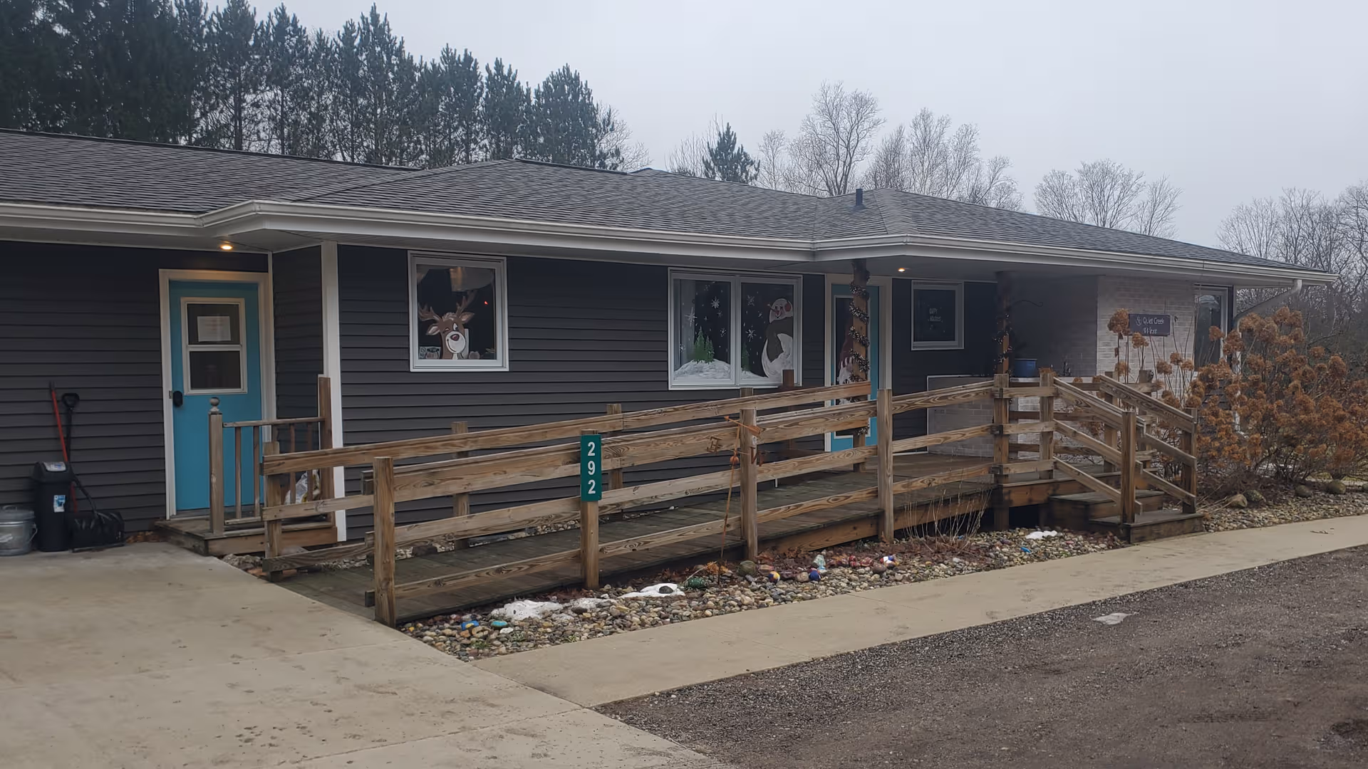 Single-story Quiet Creek AFC exterior with wooden ramp, railing, and teal front door.