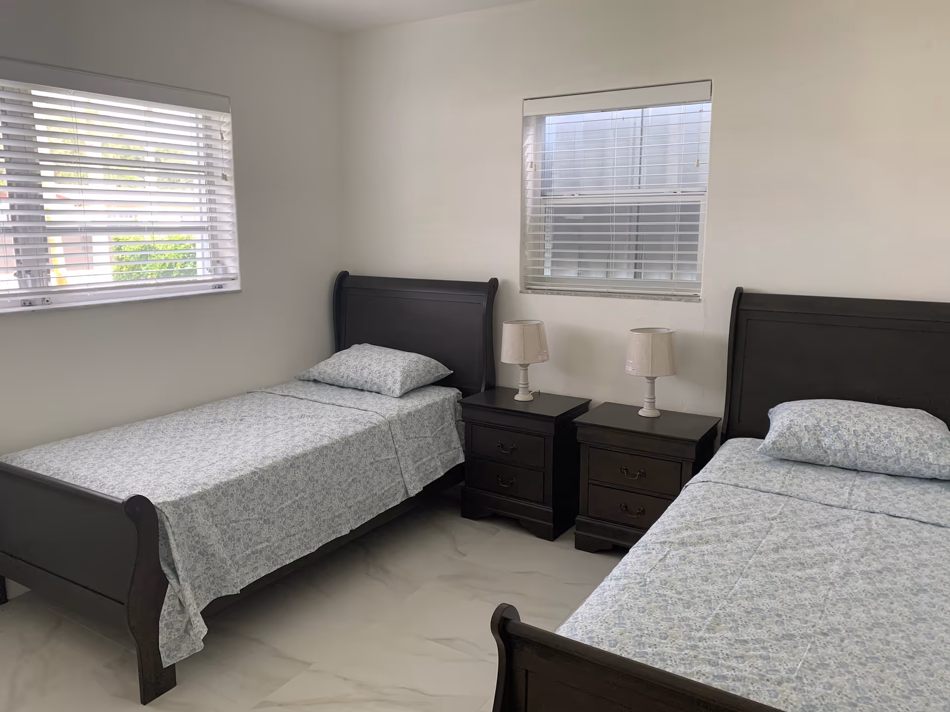 Two twin beds with matching nightstands and lamps in a bright bedroom.