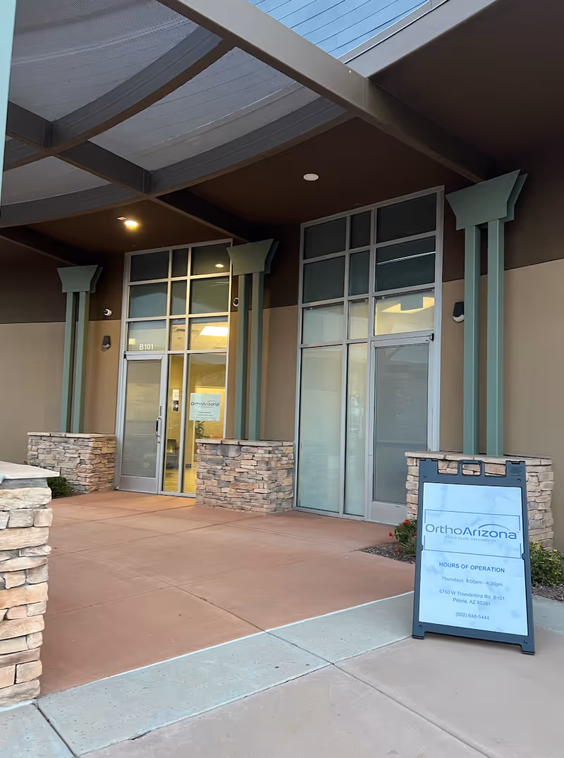Exterior view of OrthoArizona Thunderbird entrance with glass doors and stone columns.