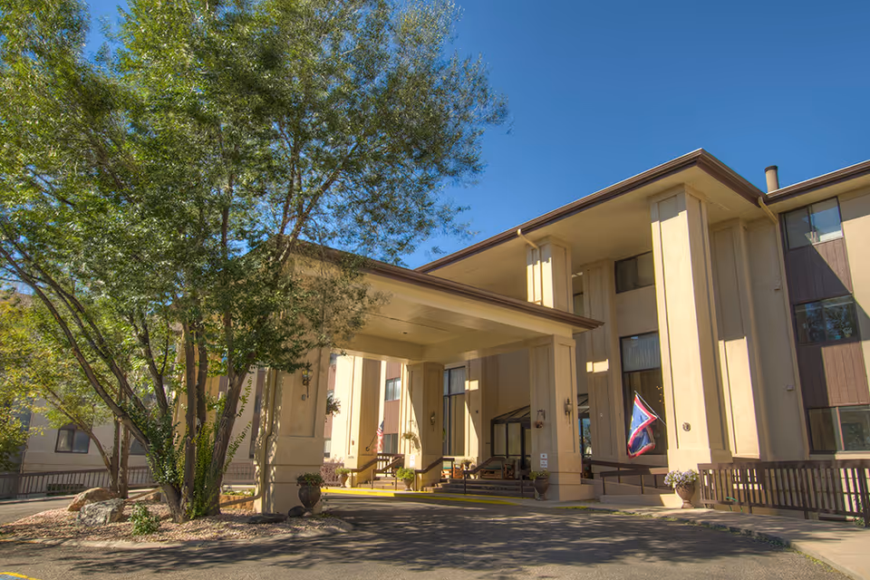 Front entrance of the Pointe Frontier senior living building with a covered porte-cochere, columns, trees and flags.