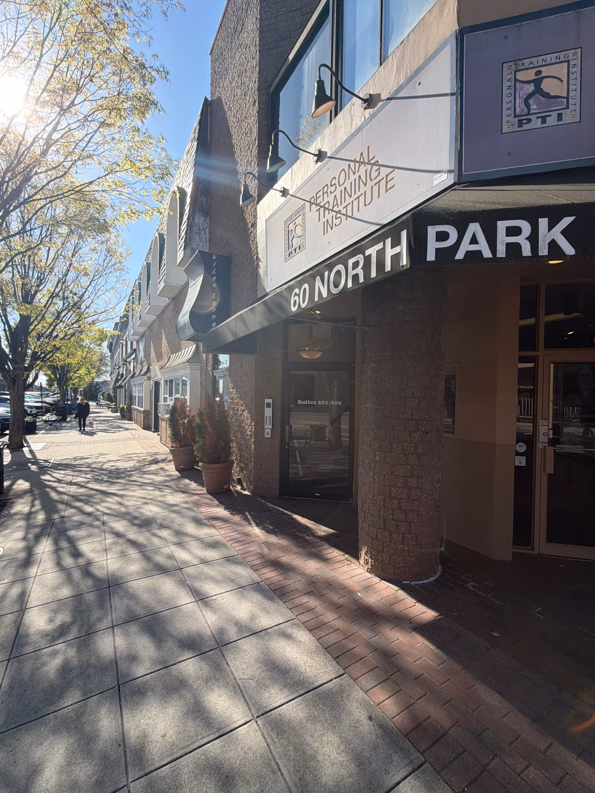 Exterior street view of a building with storefront signs and trees along the sidewalk.