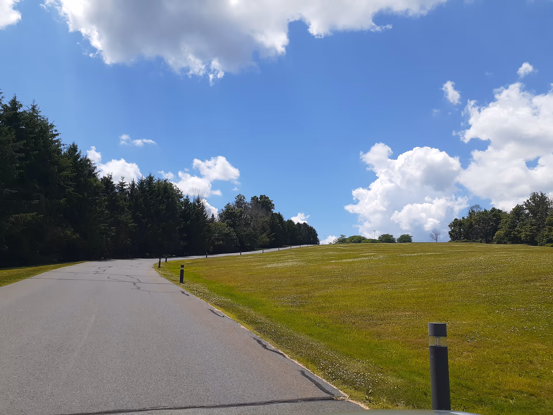 A paved road curves through a grassy landscape under a blue sky.
