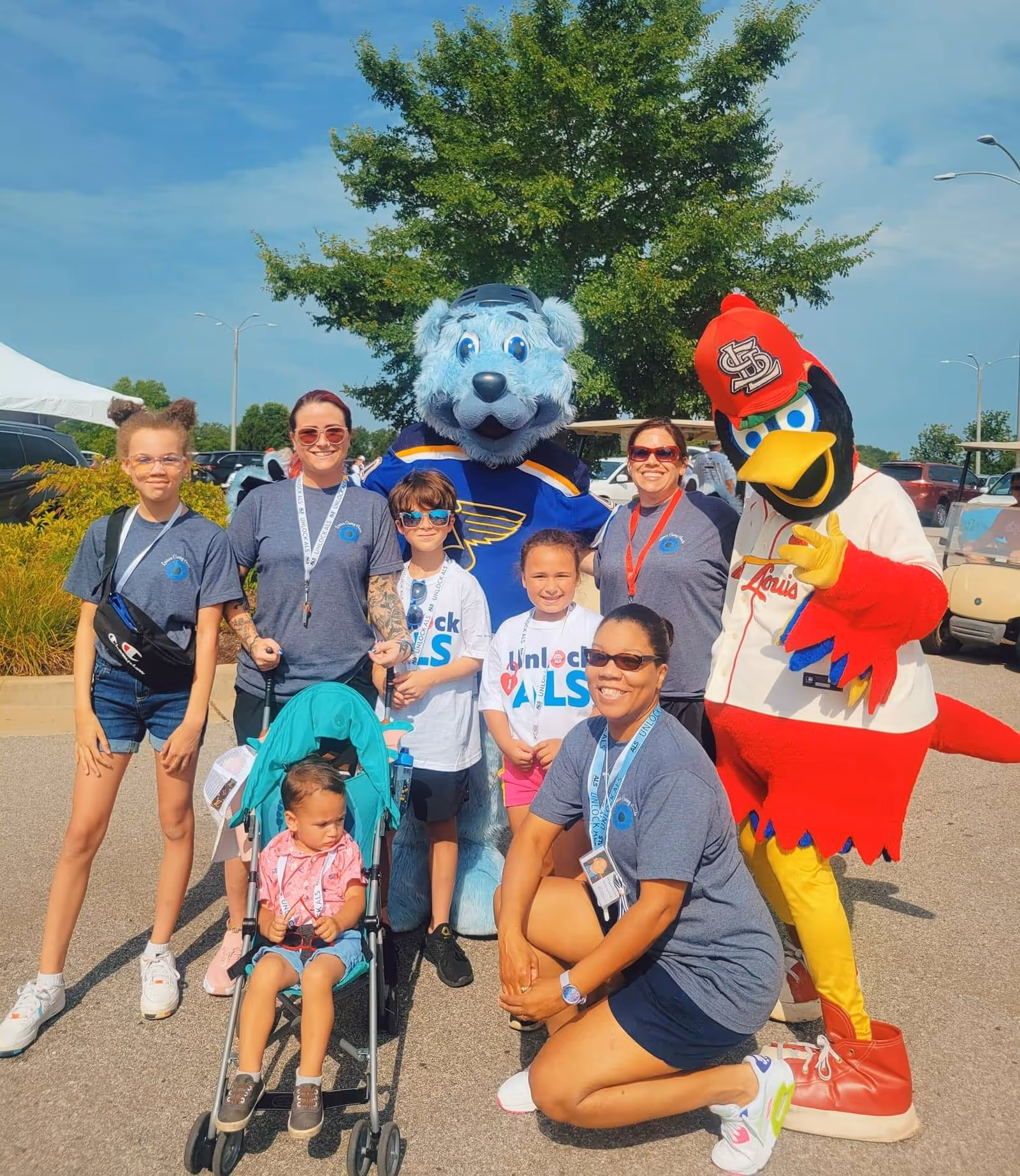 Group of staff, children, and mascots posing in a parking lot outside Louise's Caring Hands.