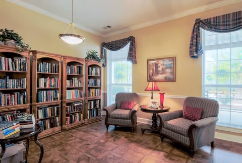 Cozy sitting area with bookshelves, two upholstered armchairs and a side table beneath large windows.