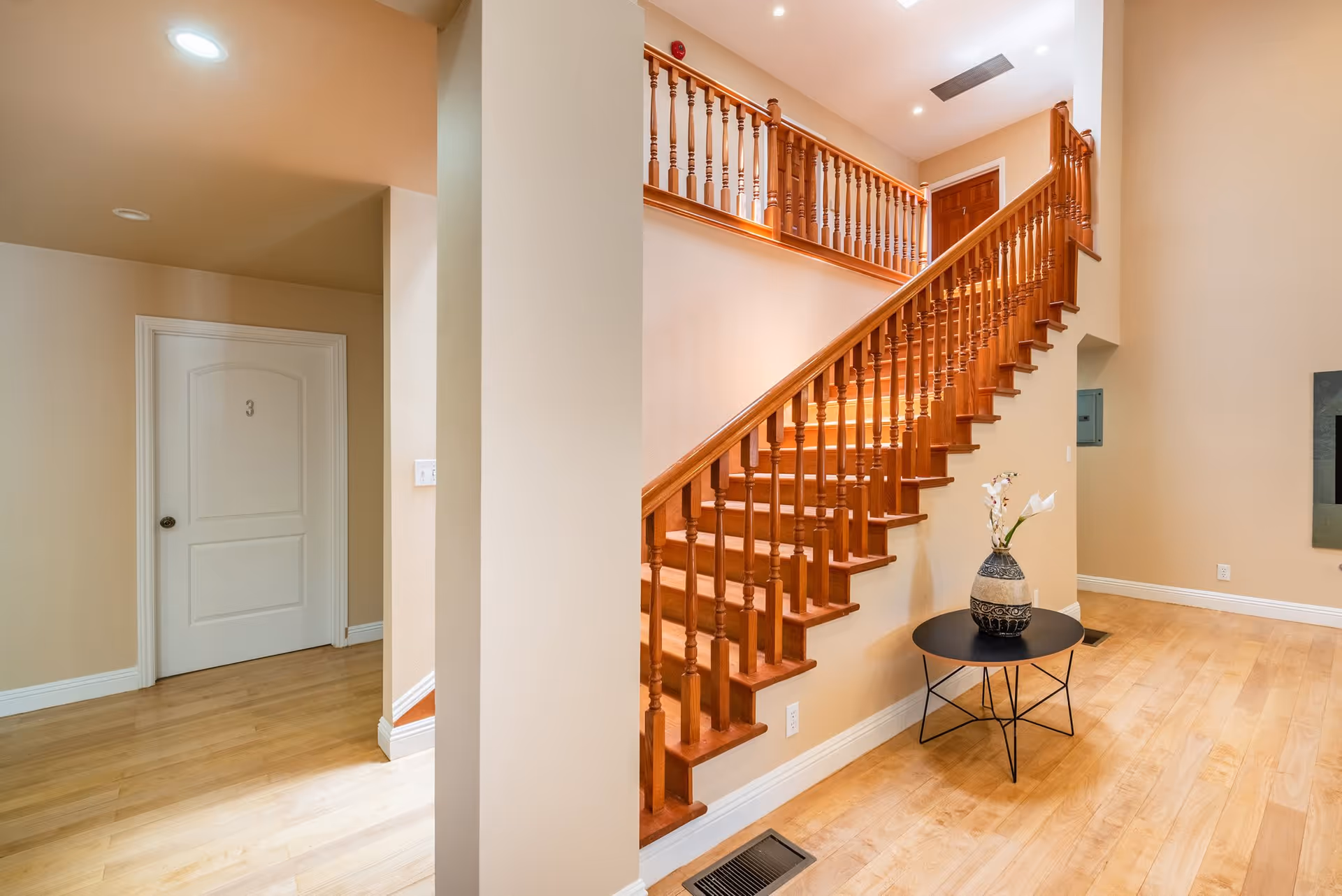 Interior hallway featuring a wooden staircase with turned balusters, a small round table with a vase, and a door numbered 3.