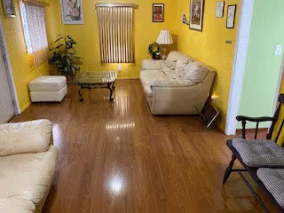 Small living room with yellow walls, wood flooring, beige sofas, a glass coffee table and a floor lamp.