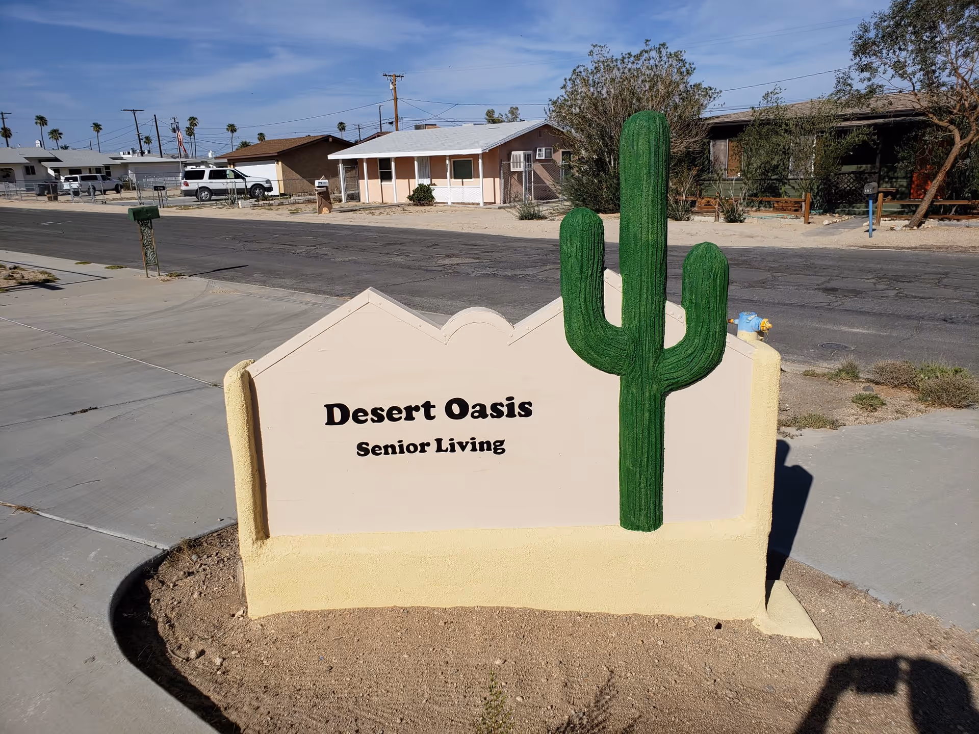 Front view of Desert Oasis Senior Living sign with a tall green cactus sculpture.