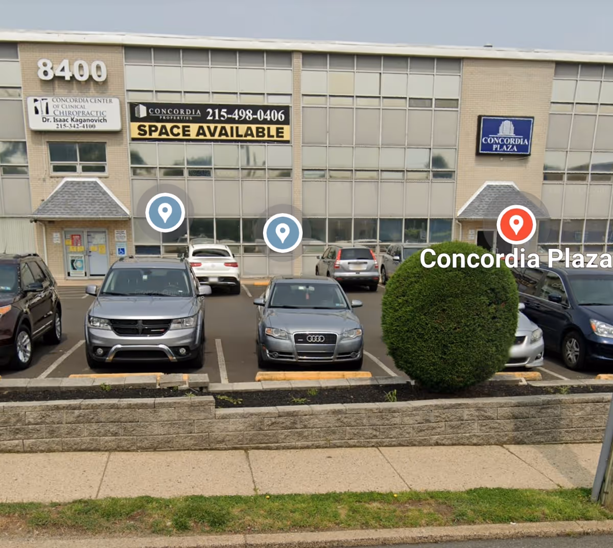 Exterior view of a storefront-style building with parked cars and signage in front
