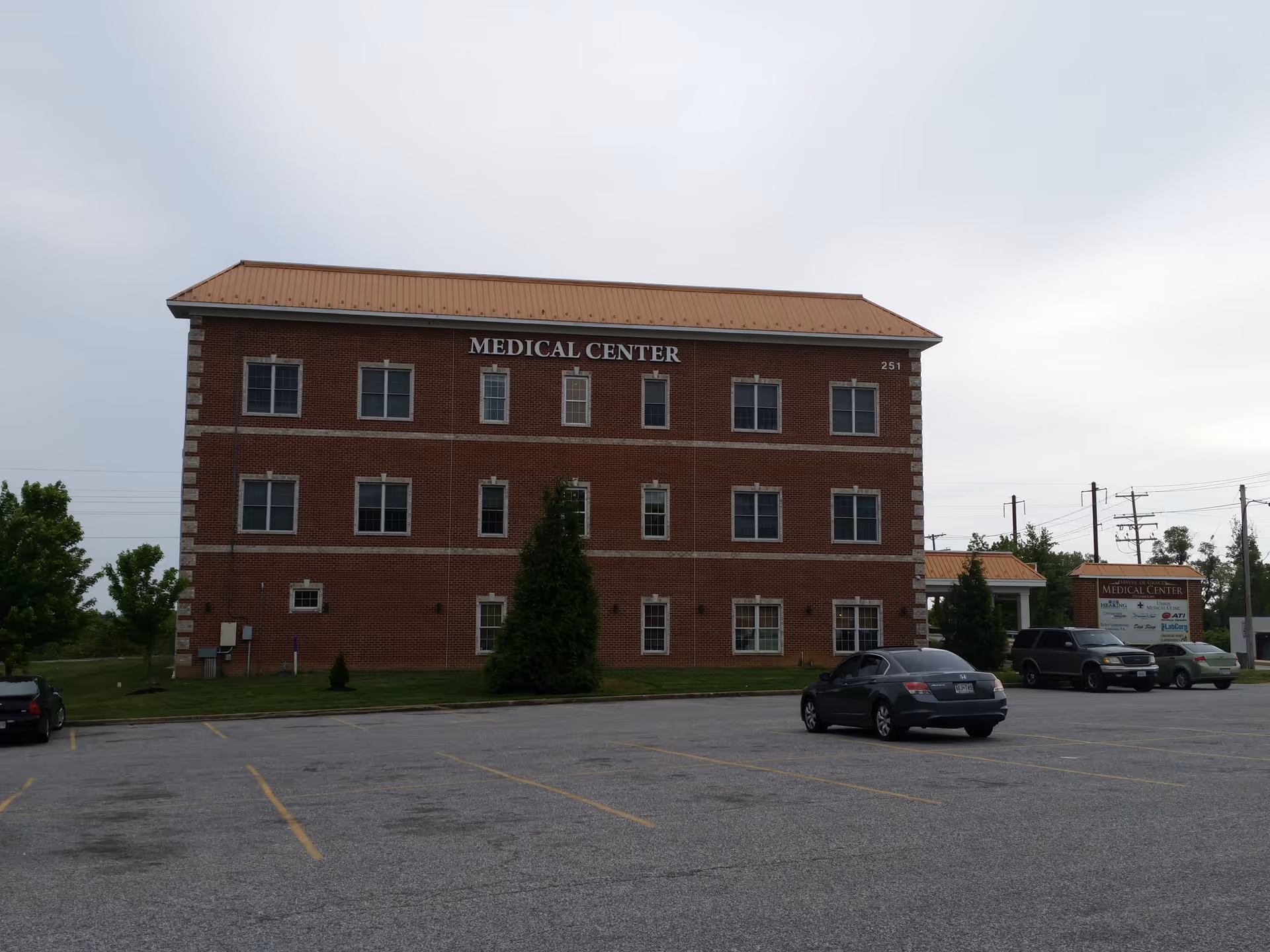 Brick medical center building with a parking lot and several cars in front.
