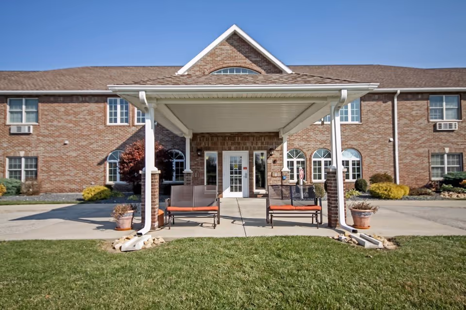 Brick senior living facility entrance with a covered porch and outdoor seating.