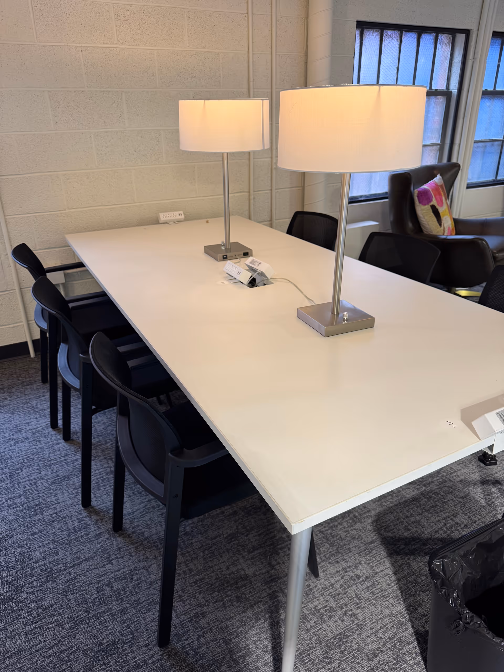 A long white conference table with lamps and black chairs in a bright room.