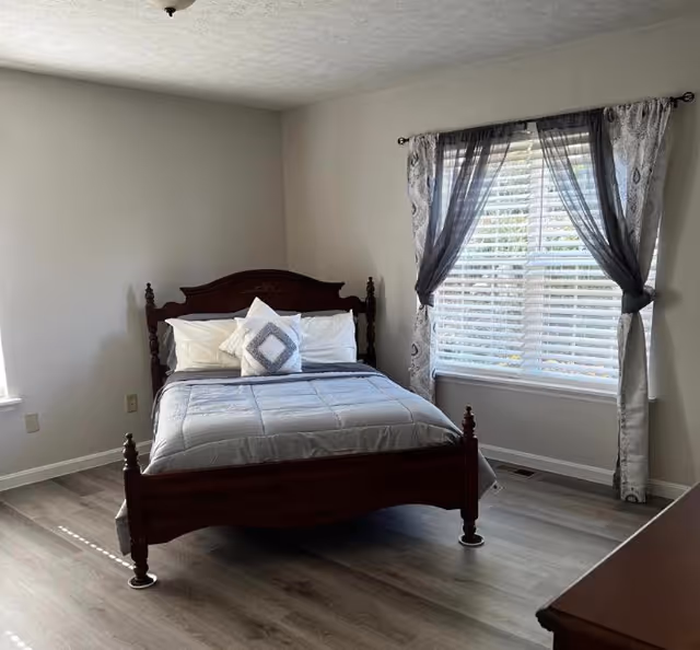 A bedroom with a wooden bed, gray walls, and a window with curtains.
