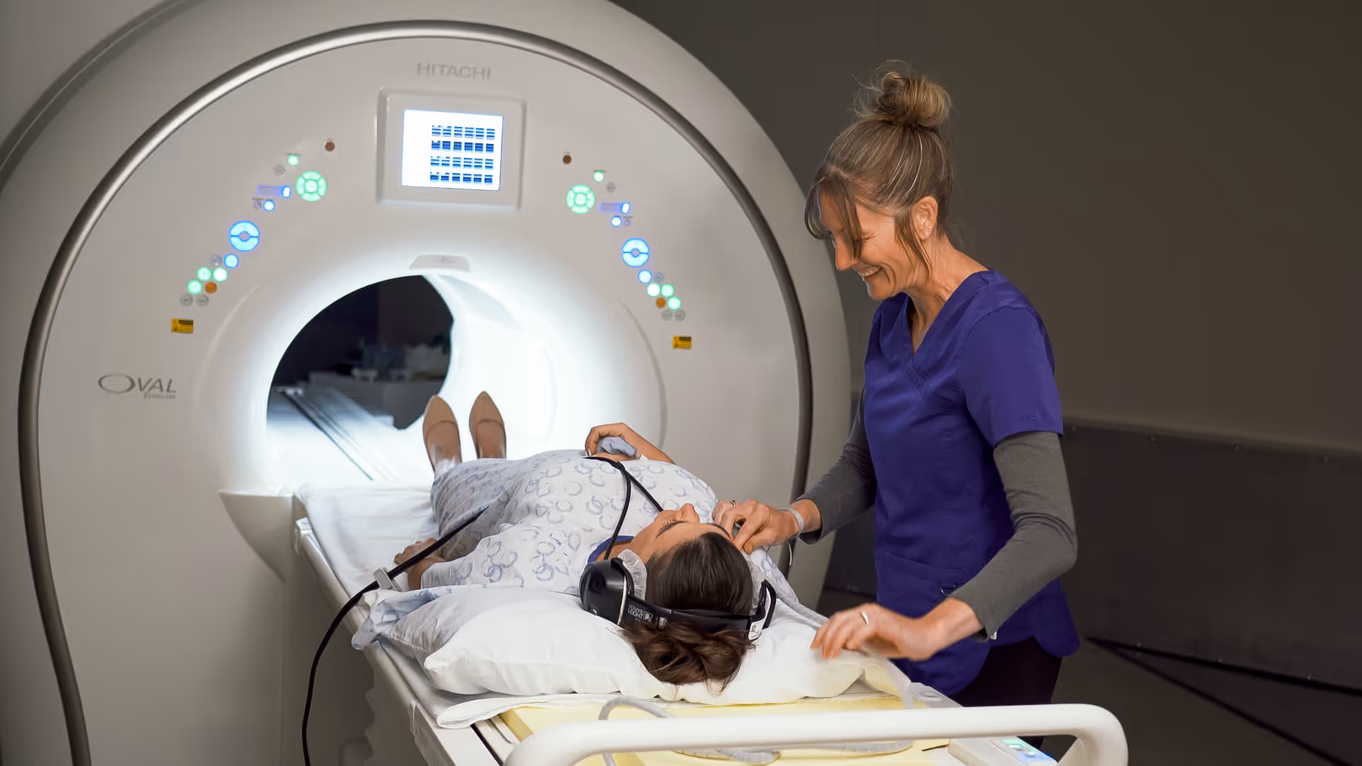 A patient lies on an MRI table while a nurse prepares beside a large imaging scanner.