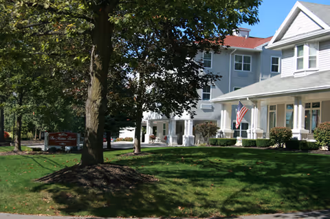 Front exterior of a multi-story residential building with a porch, American flag, green lawn and trees.