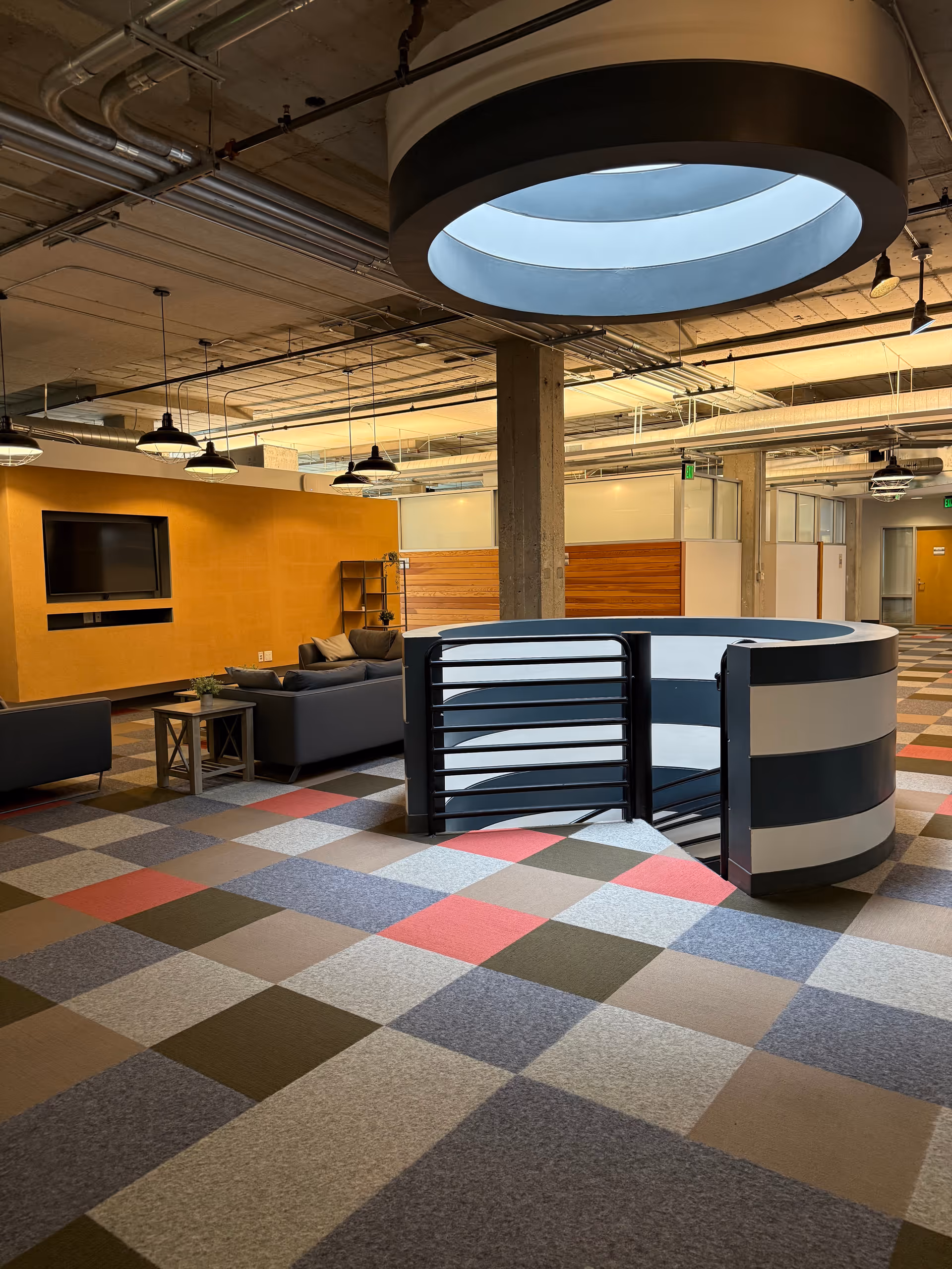Modern indoor common area with sofas, wall TV, orange accent wall, circular railing.