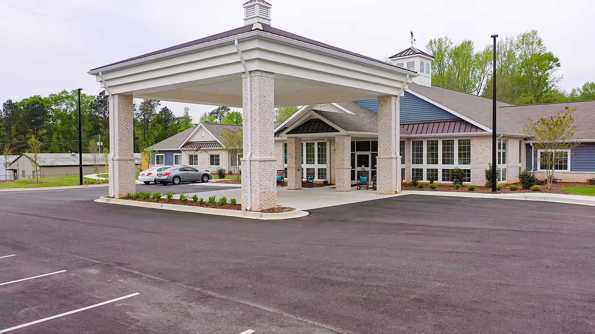 Exterior view of a senior living facility entrance with a large covered porte-cochere and parking.