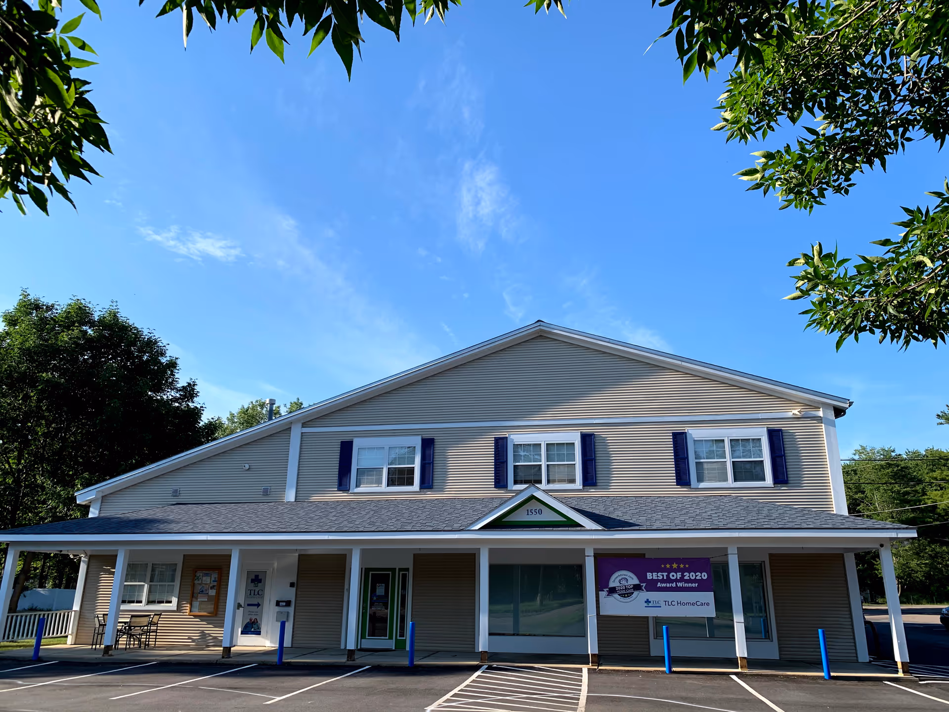 Two-story beige building with blue shutters and a covered entrance under a clear blue sky.