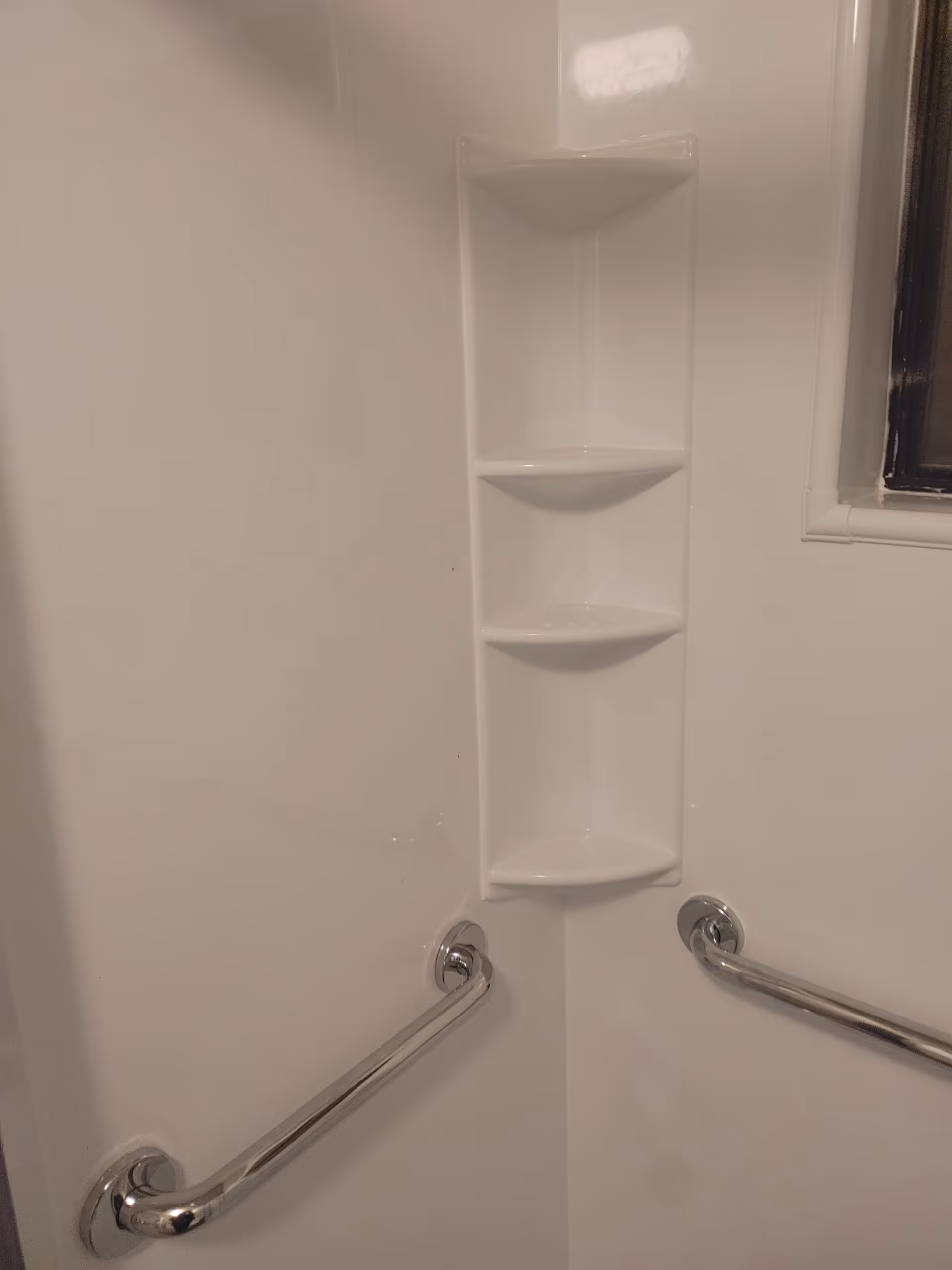 White shower stall with built-in corner shelves and two chrome grab bars.
