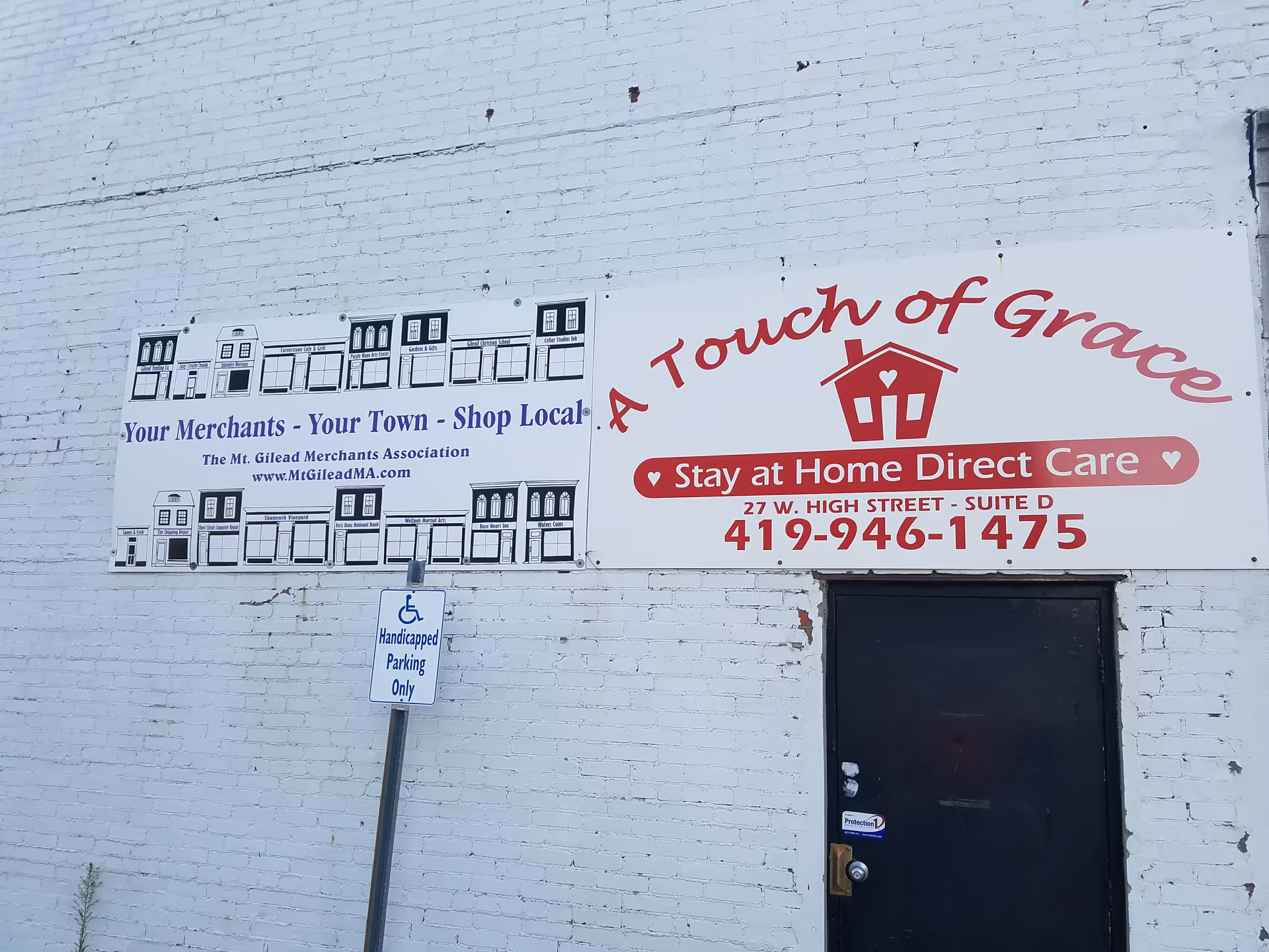White brick building exterior with a large A Touch of Grace sign and a dark door.