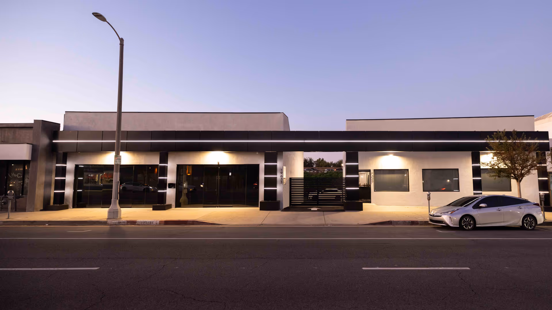 Modern single-story building storefront along a street with a parked silver car.