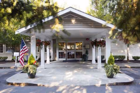 Front entrance of Aegis Living Issaquah with columns, plants, and American flag