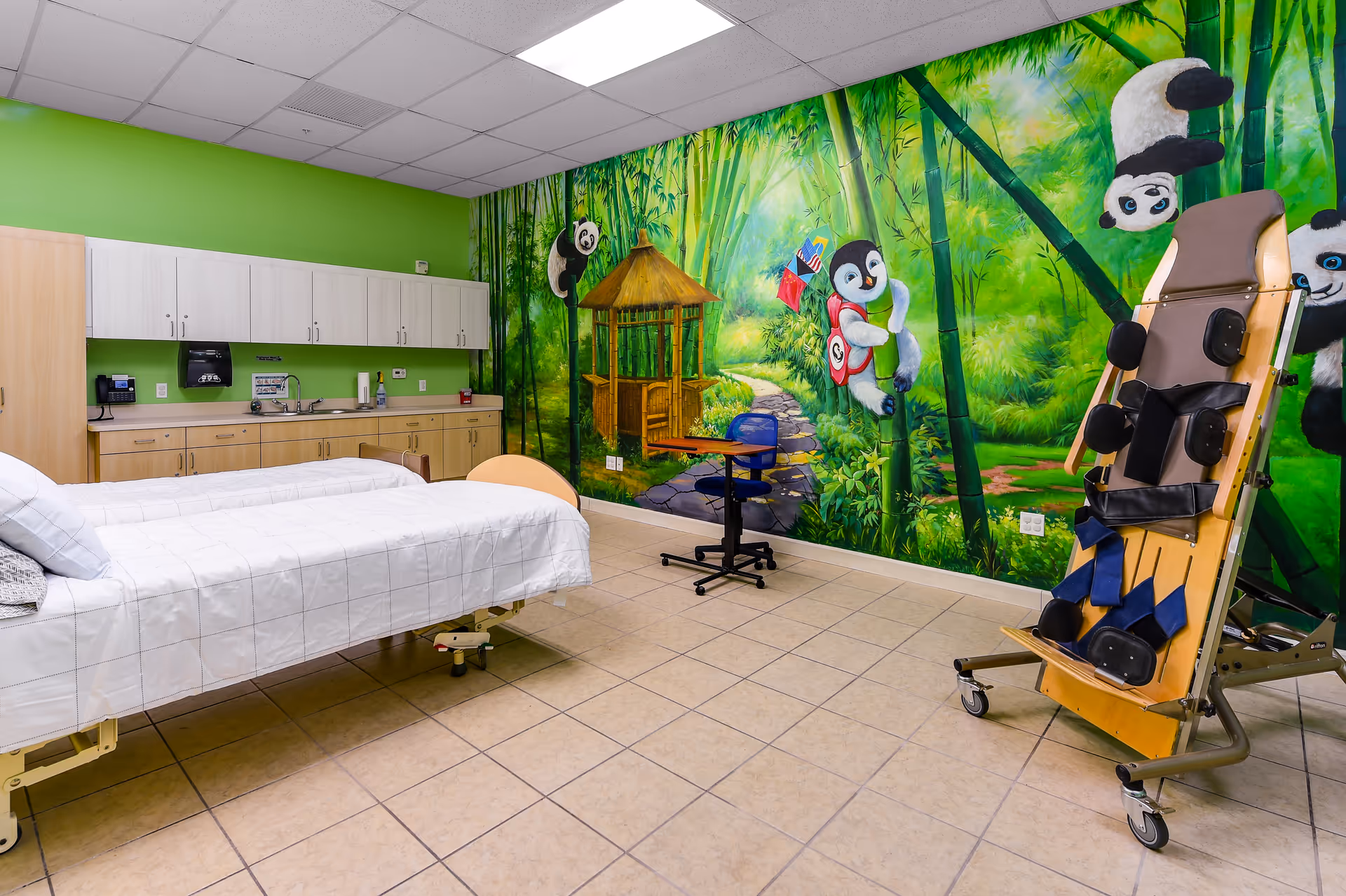 Bright interior treatment room with a hospital bed, cabinetry, and a panda-themed jungle mural