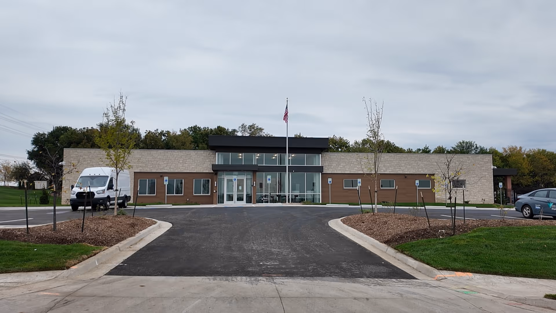 Front view of Midland Care PACE facility with driveway, parking, and flagpole.