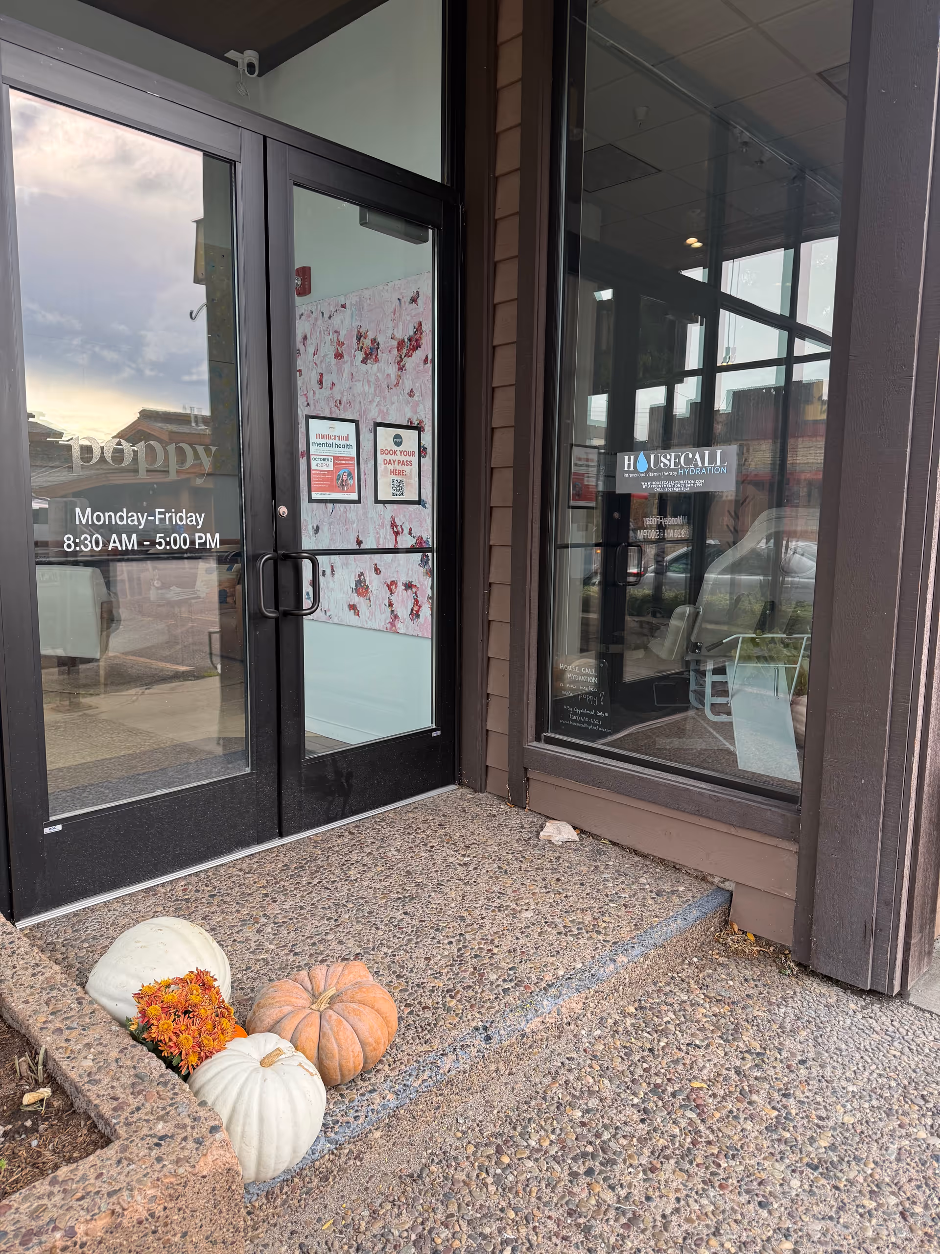 Exterior entrance to House Call Hydration facility with glass doors, pumpkins, and fall flowers.