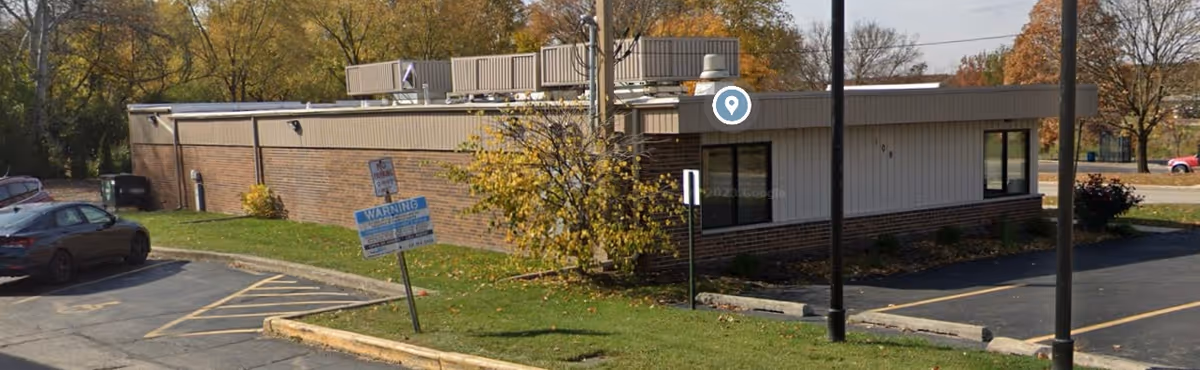 Exterior view of a single-story facility with brick and metal siding, parking, and fall trees.