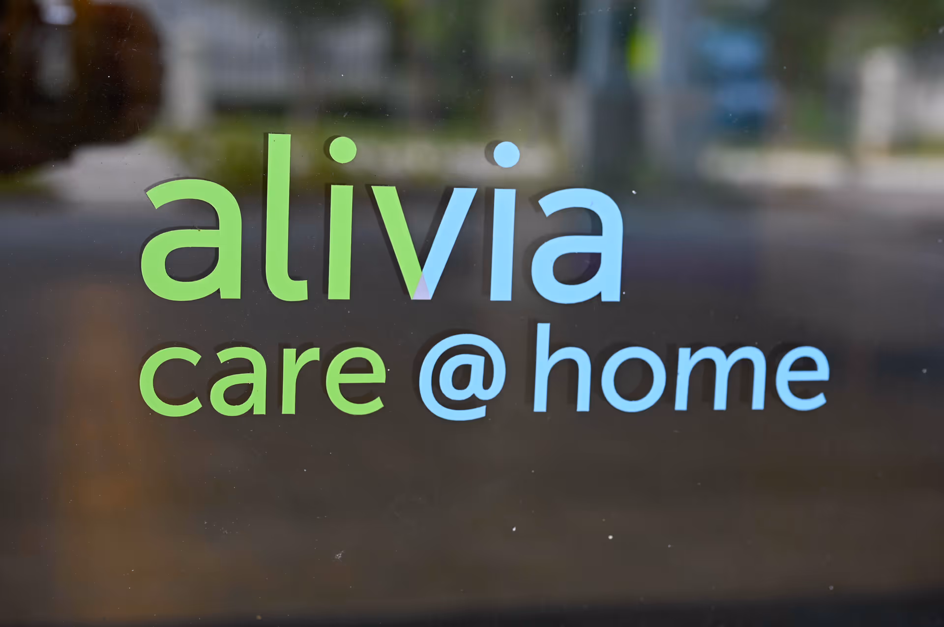 Glass door with gradient alivia care @ home logo and blurred exterior