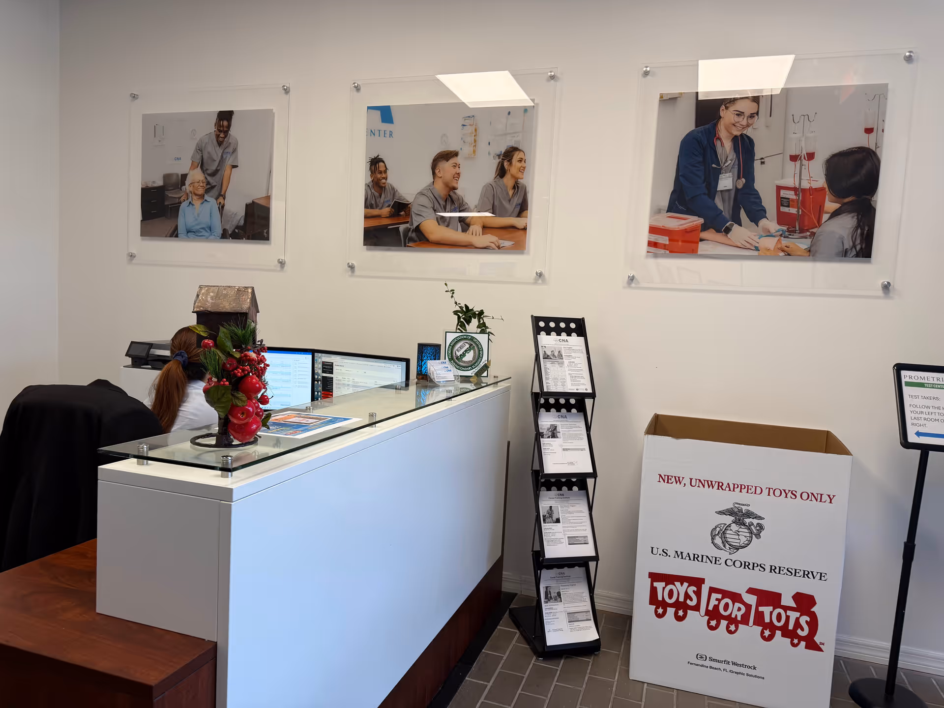 Reception area with a white counter, framed photos, brochure rack, and Toys for Tots box.