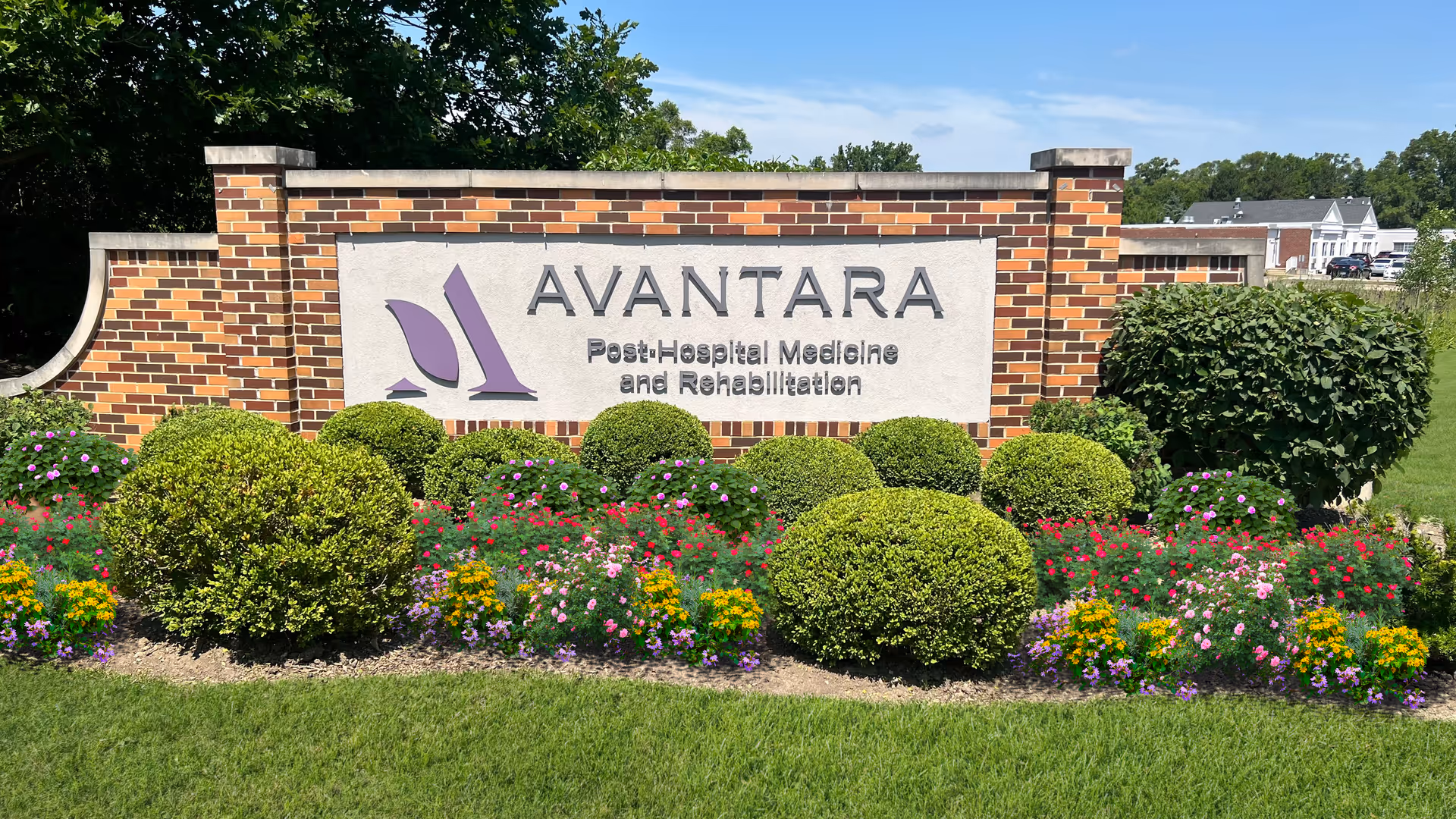 A brick AVANTARA sign with trimmed shrubs and colorful flowers in front.