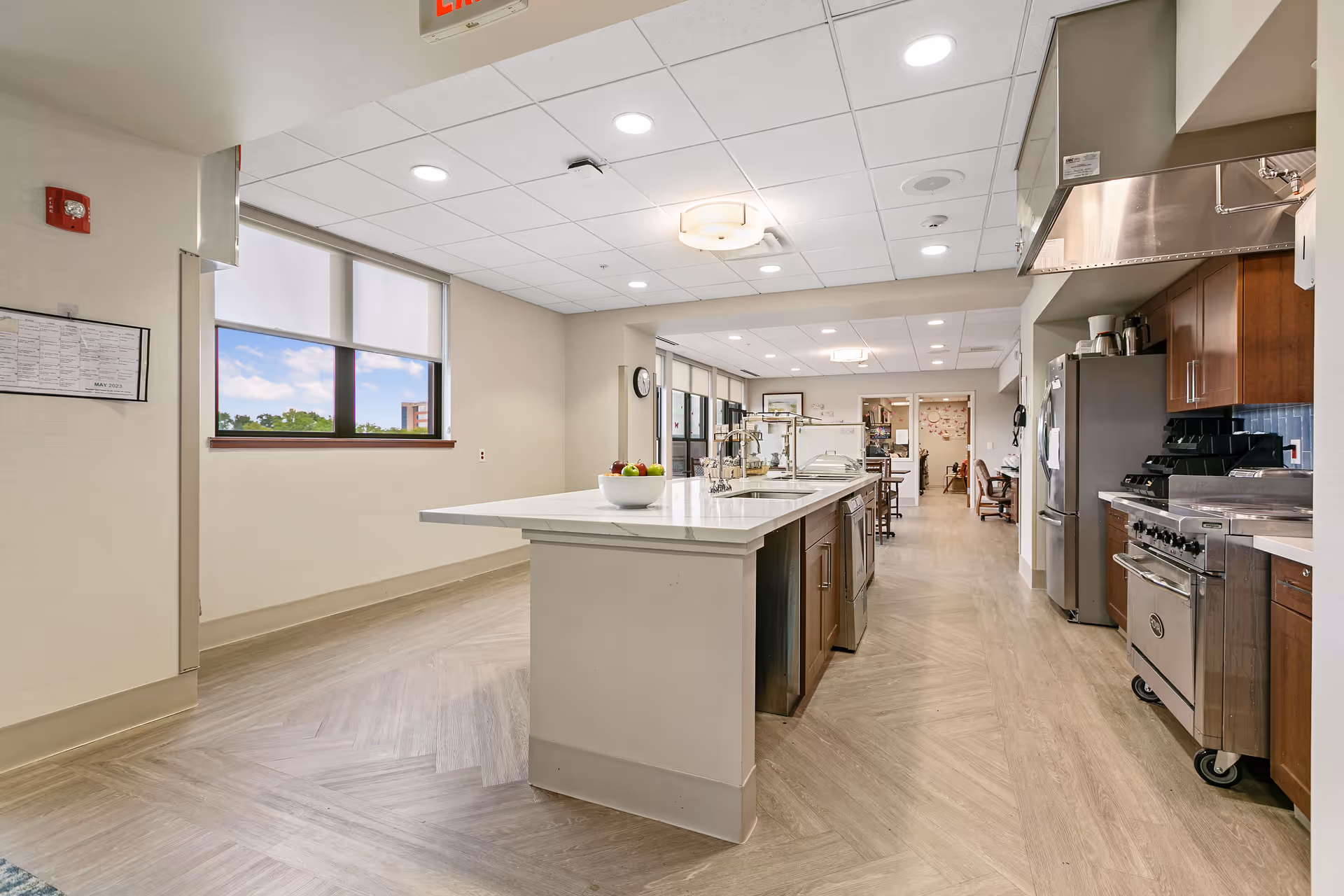 Bright commercial kitchen with central island, stainless appliances, and overhead lighting.