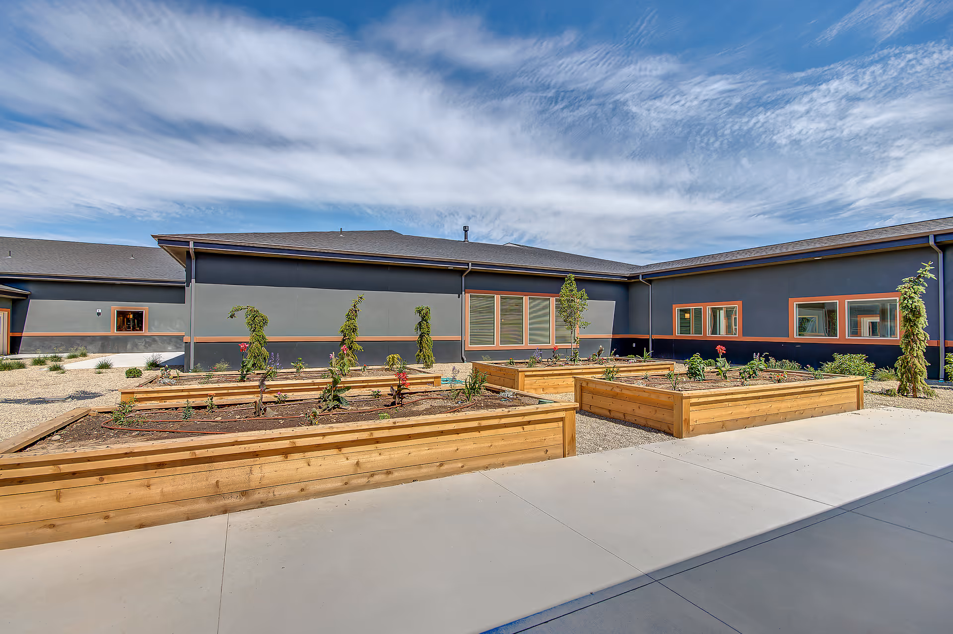 Exterior view of Grace Assisted Living Caldwell showing raised wooden planters and a bright blue sky.