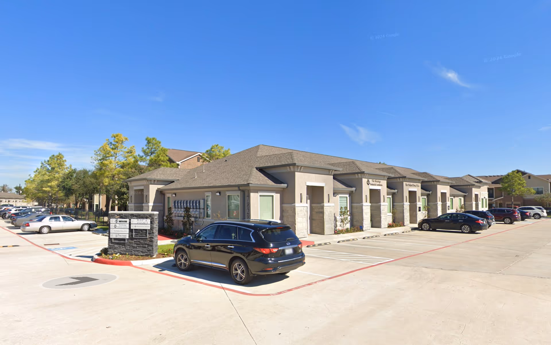 Exterior view of a single-story senior living complex with parked cars and blue sky.