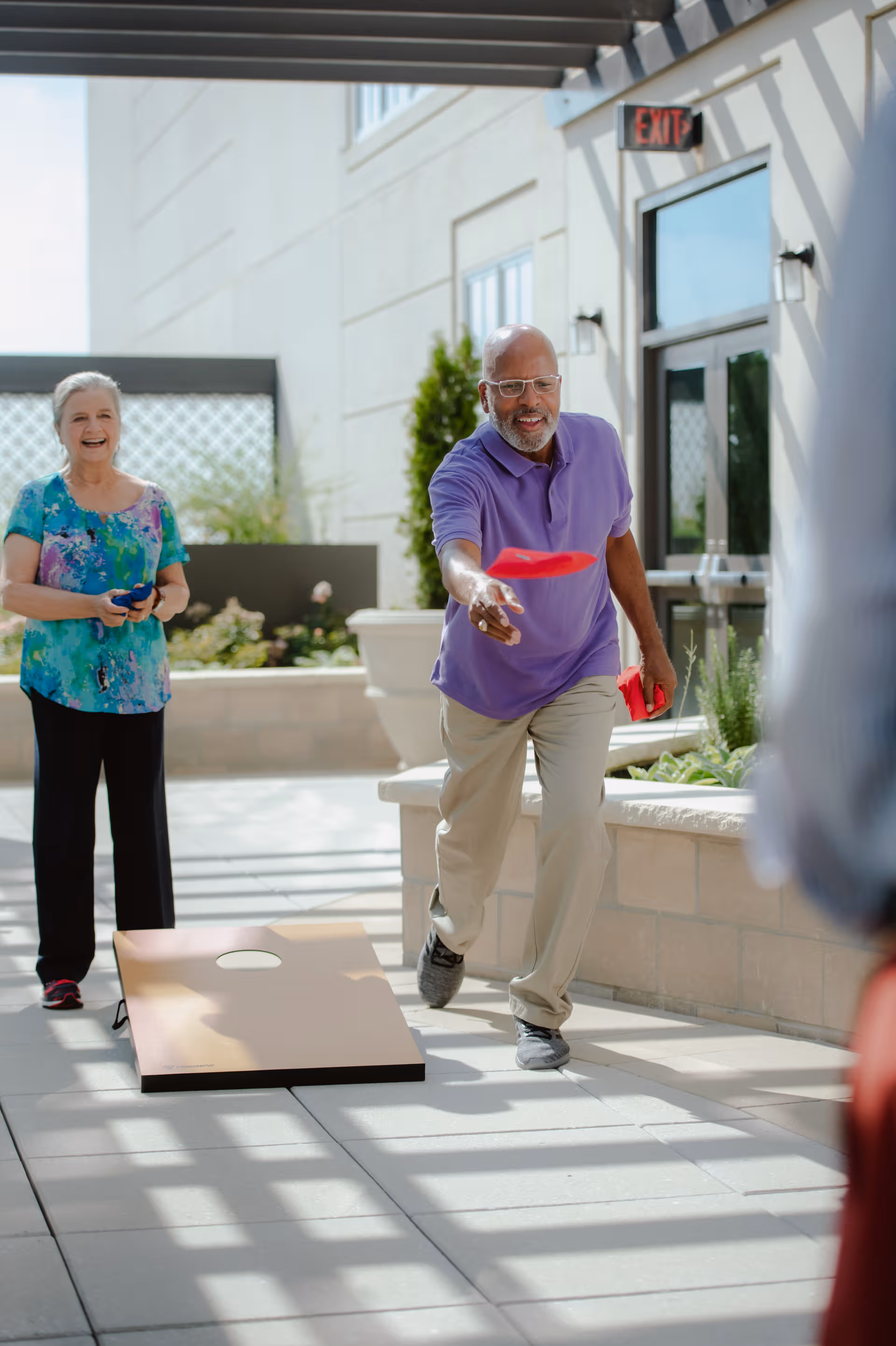 Two seniors play cornhole outdoors in a Briar Creek Health Center courtyard.