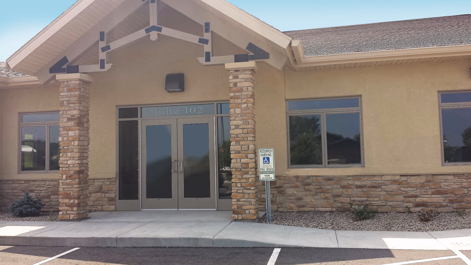 Entrance to a senior living facility with glass doors, stone columns, and a parking area.