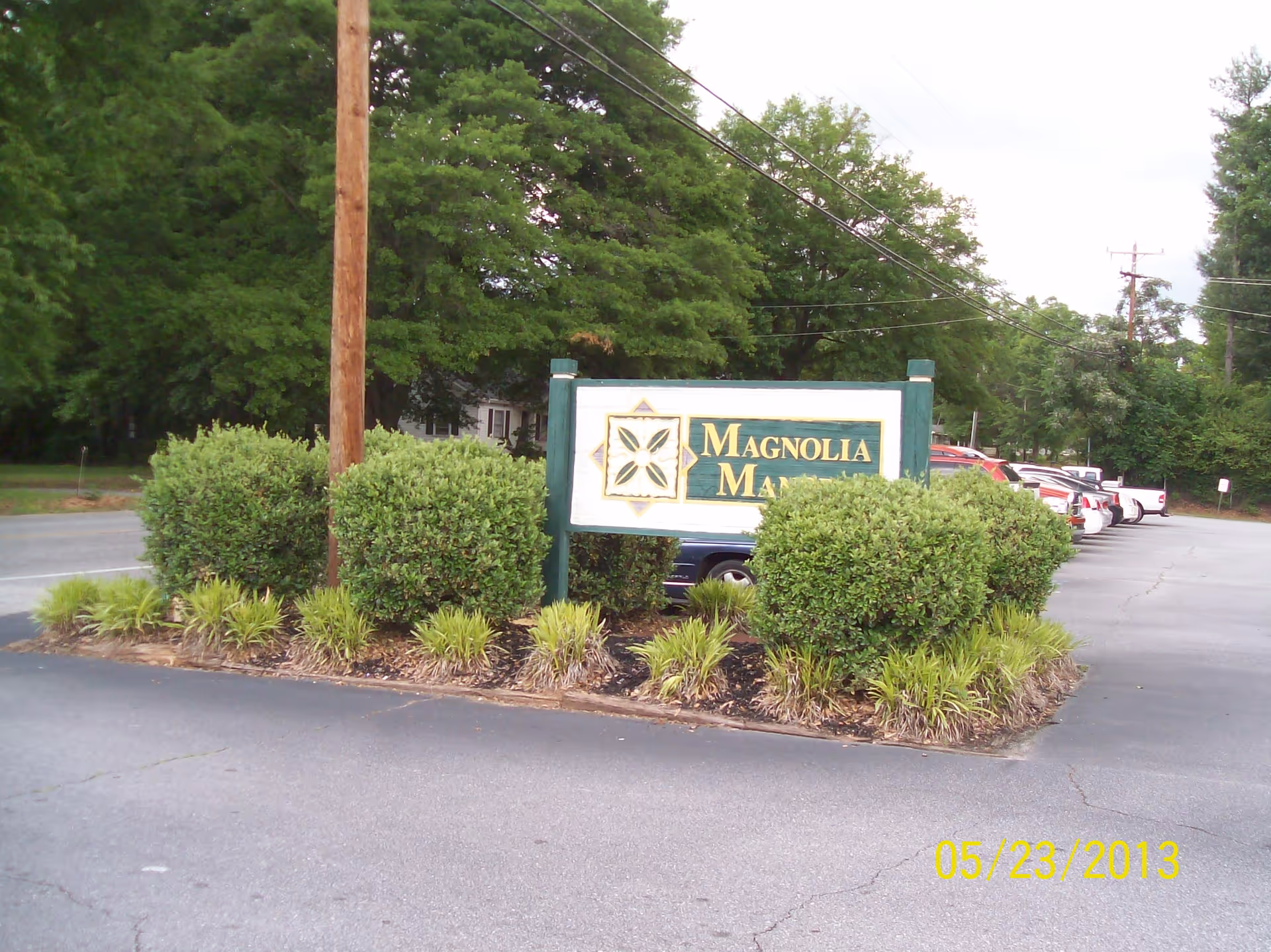 Exterior view of Magnolia Manor sign with greenery and parked cars along the front entrance.