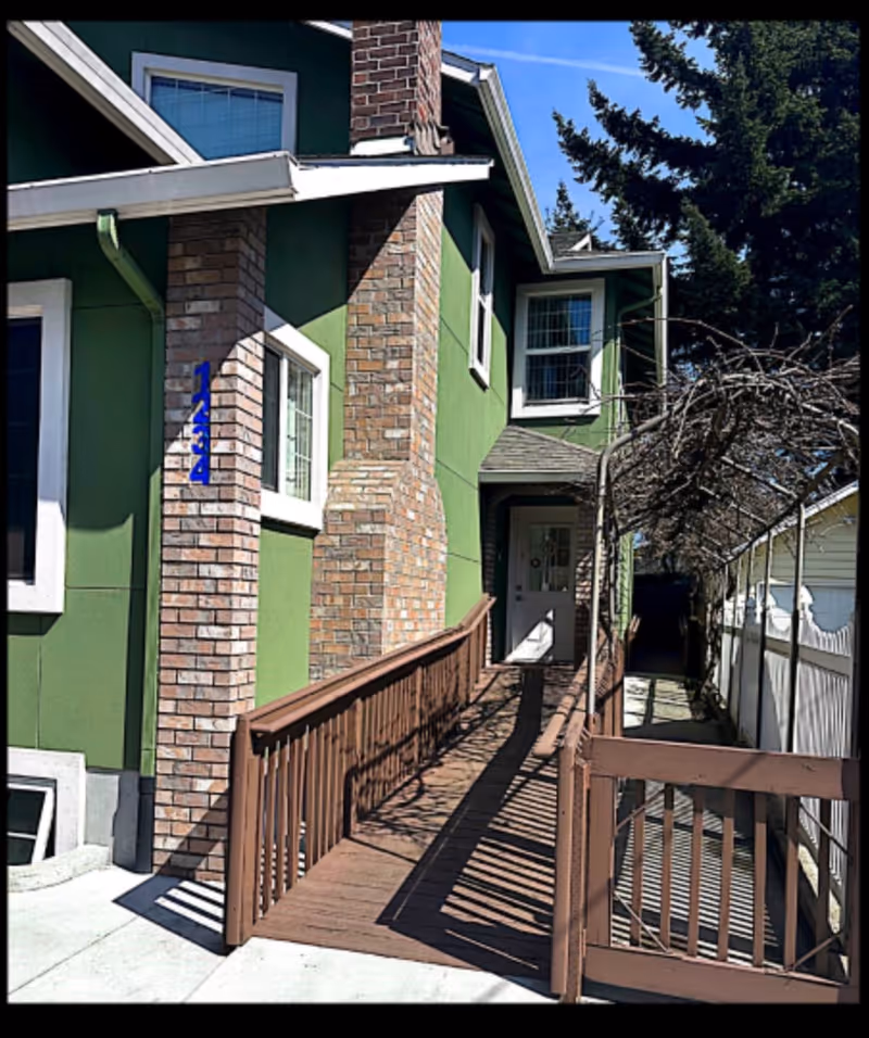 Green building exterior with brick columns and a wooden ramp leading to a front door.