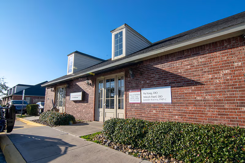 Brick medical clinic exterior with glass doors, signage, and landscaped shrubs.