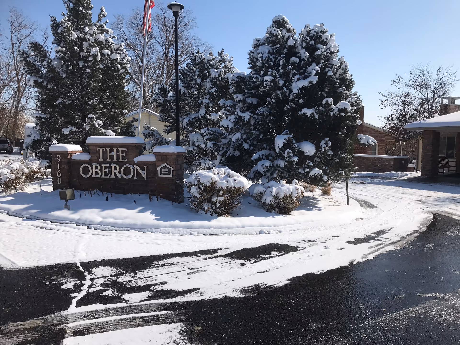 Snow-covered entrance sign for The Oberon with trees and a curved driveway