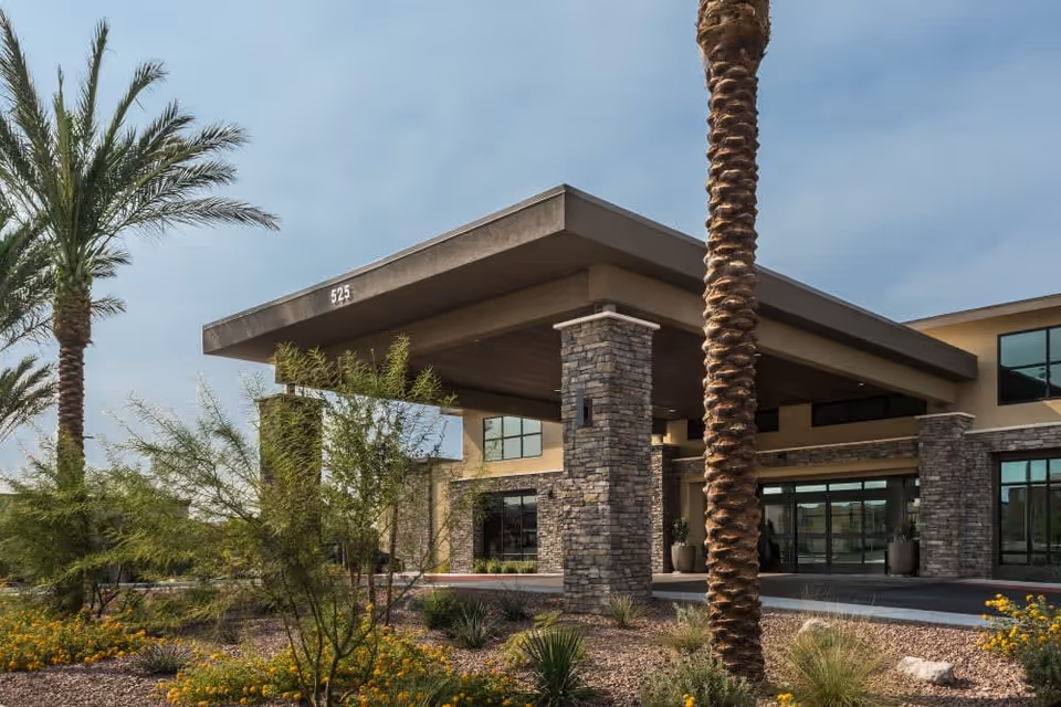 Front entrance of Carnegie Heights at Henderson with a covered porte-cochere, stone pillars, palm trees and desert landscaping.