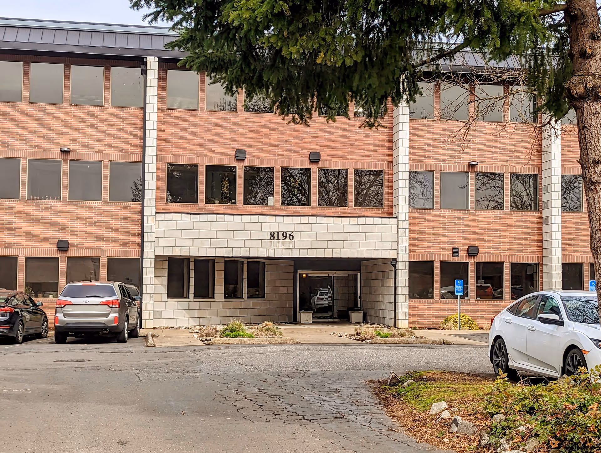 Brick hospice building with large windows and a central entrance, parked cars in front.