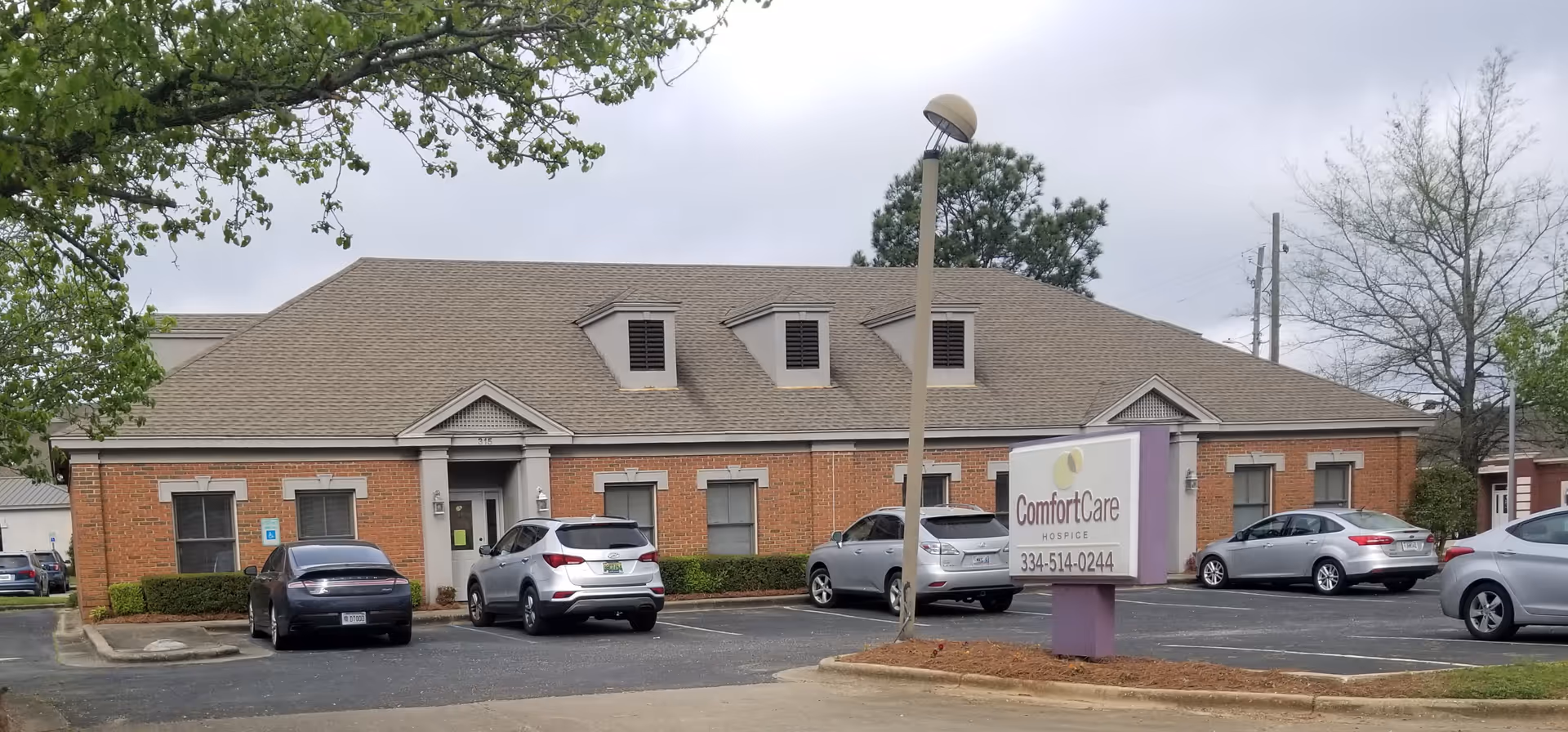 Front view of a single-story brick hospice building with a parking lot.