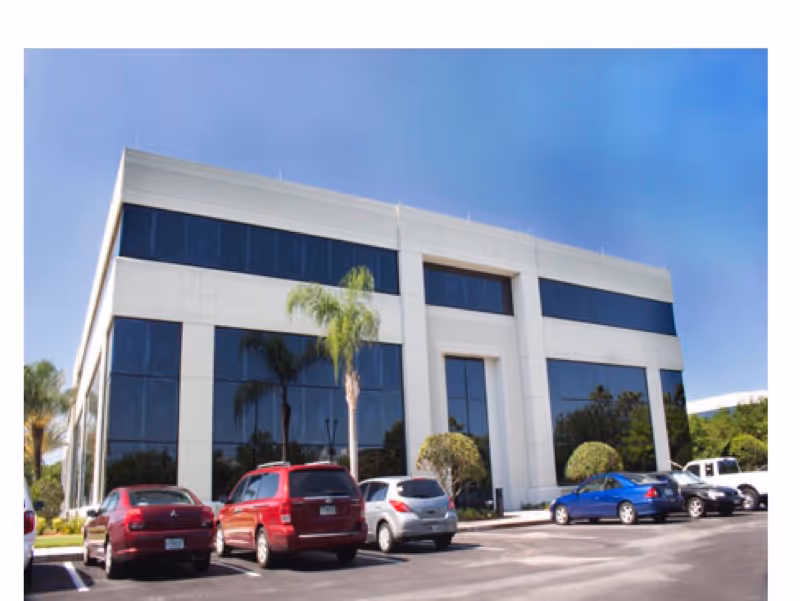 Modern exterior of a white building with large glass windows and multiple parked cars.