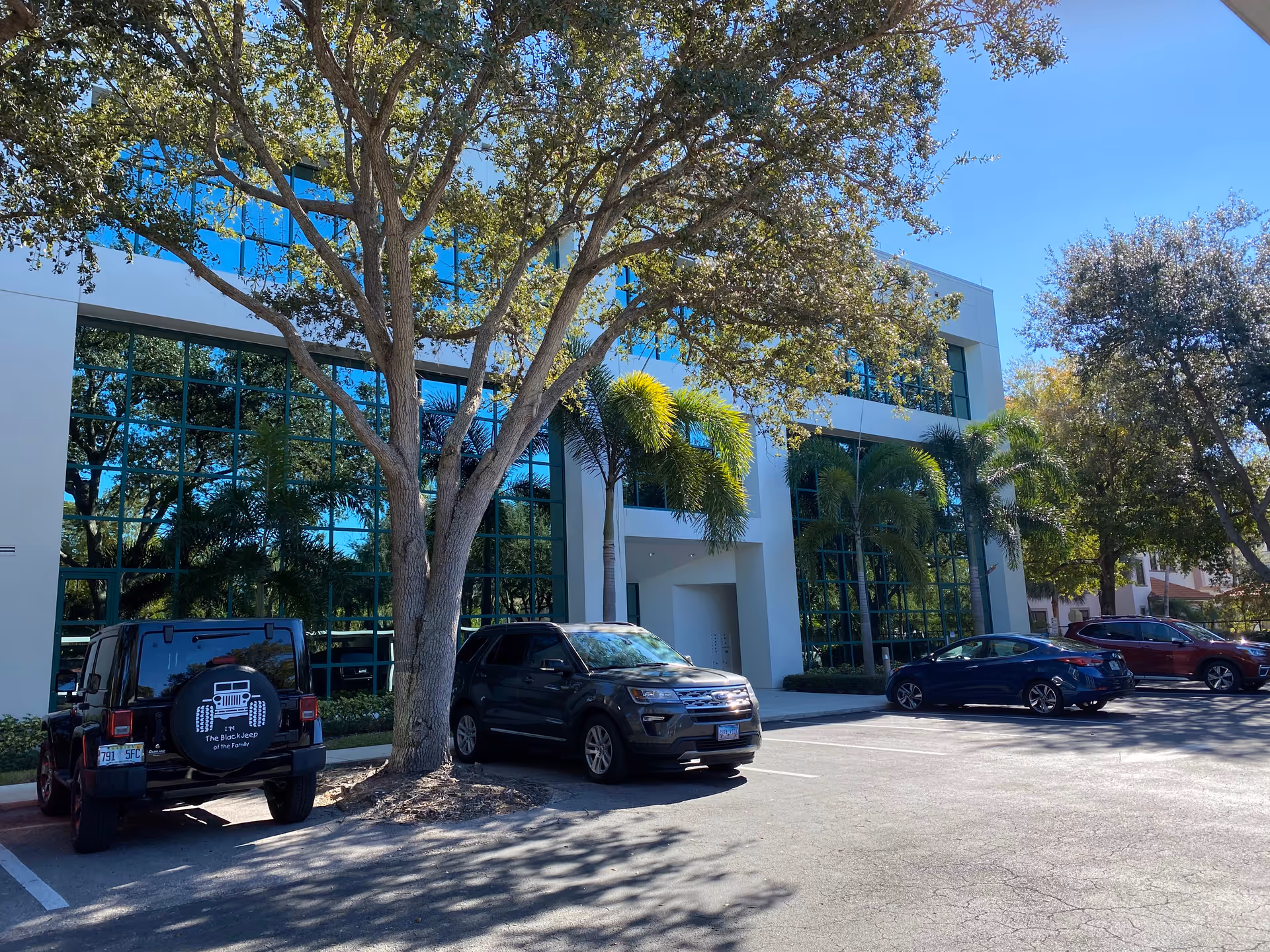 Modern two-story facility with blue-tinted glass, trees, and several parked cars in the lot.